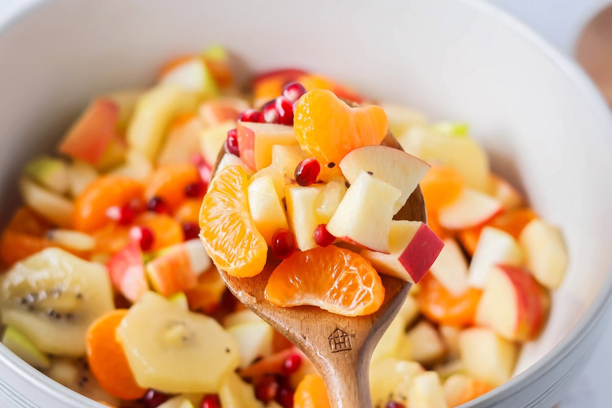 Bright and refreshing, this winter fruit salad blends clementines, kiwi, apples, pear, and pomegranate with a light citrus honey dressing. Mixing the fruit and honey citrus dressing together.