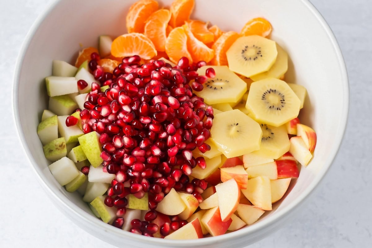Bright and refreshing, this winter fruit salad blends clementines, kiwi, apples, pear, and pomegranate with a light citrus honey dressing. Clementines, pear, apples, pomegranate seeds, and kiwis in a bowl.