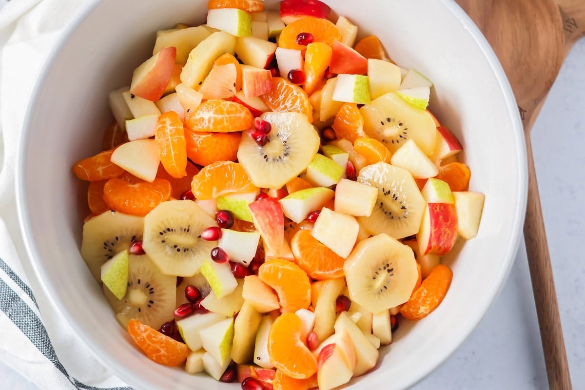 Bright and refreshing, this winter fruit salad blends clementines, kiwi, apples, pear, and pomegranate with a light citrus honey dressing. Winter fruit salad in a large white bowl.