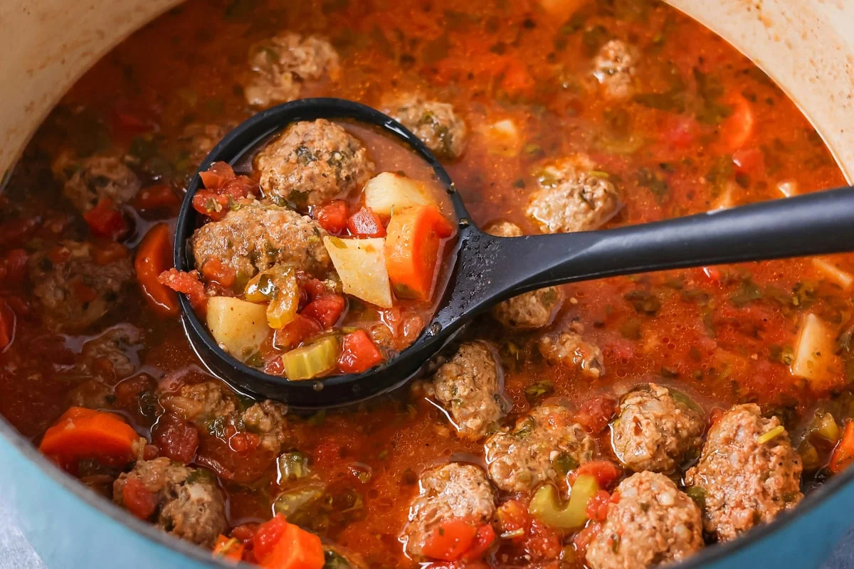 Scoop of Albondigas soup being dished out of pot.