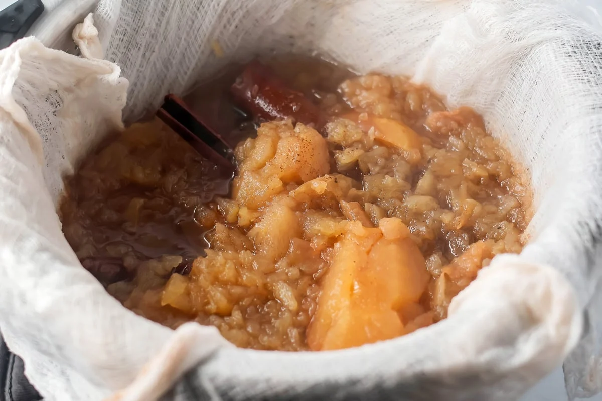 Apple cider ingredients being strained through a fine-mesh strainer.