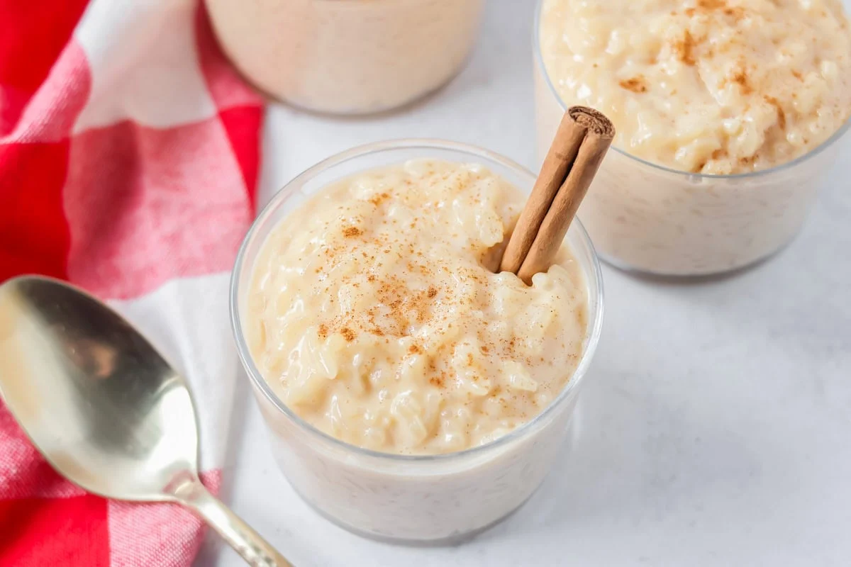 Arroz con leche recipe spooned into clear cups with a cinnamon stick in it.