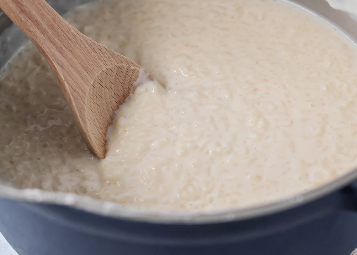 Adding milks to the rice mixture in a pan on the stove.