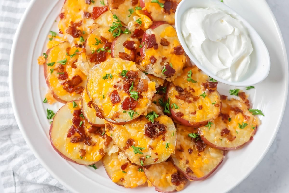 Loaded baked potato rounds with cheese and bacon stacked on white plate.