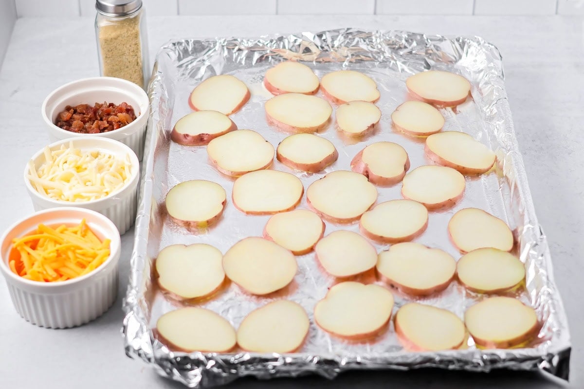 Thin sliced red potatoes on foil-lined baking sheet.