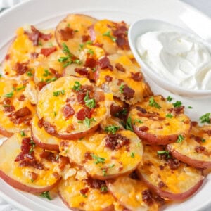 Baked potato rounds loaded with cheese, bacon and more stacked on white plate.