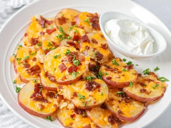 Baked potato rounds loaded with cheese, bacon and more stacked on white plate.