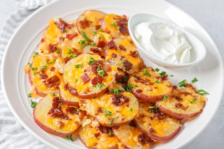 Baked potato rounds loaded with cheese, bacon and more stacked on white plate.