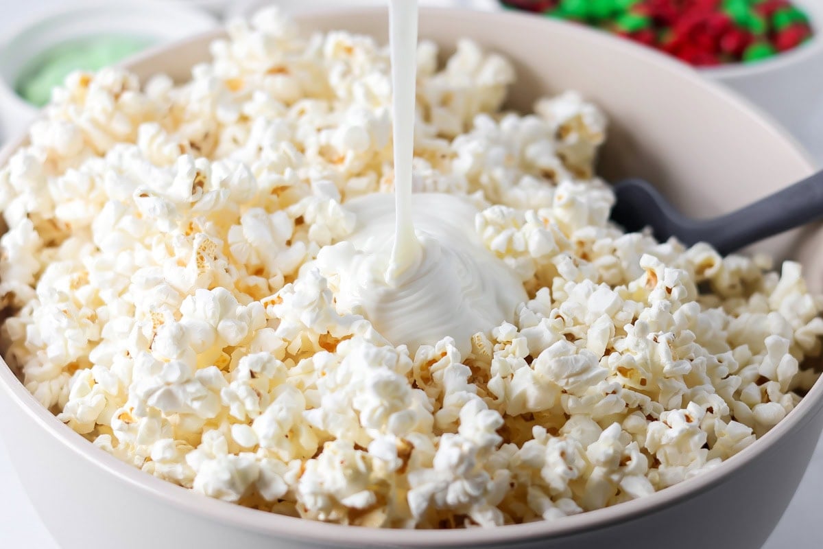 Melted white chocolate being poured over popcorn in bowl.