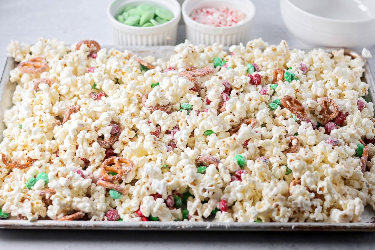 White chocolate setting on holiday popcorn on baking sheet.