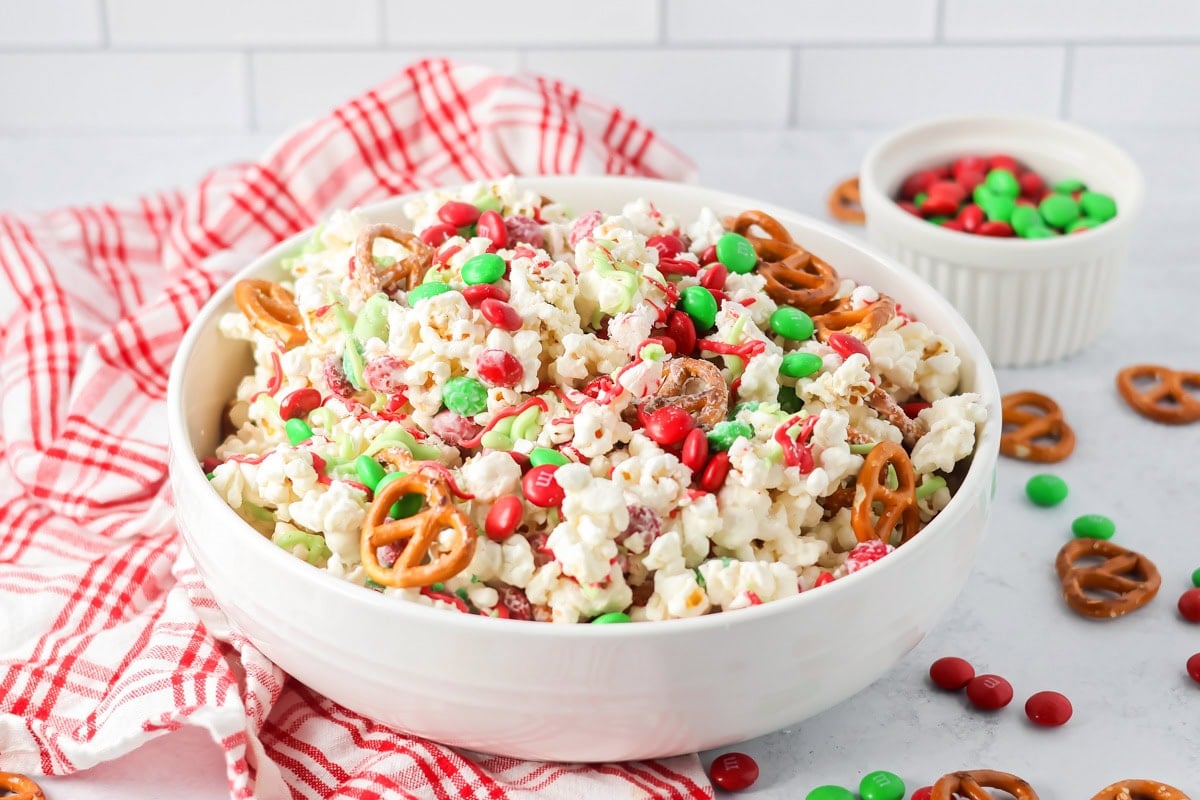 White chocolate smothered Christmas popcorn is studded with M&Ms and crushed candy canes for perfect holiday snacking in only 20 minutes! Christmas popcorn mixed together in white bowl.