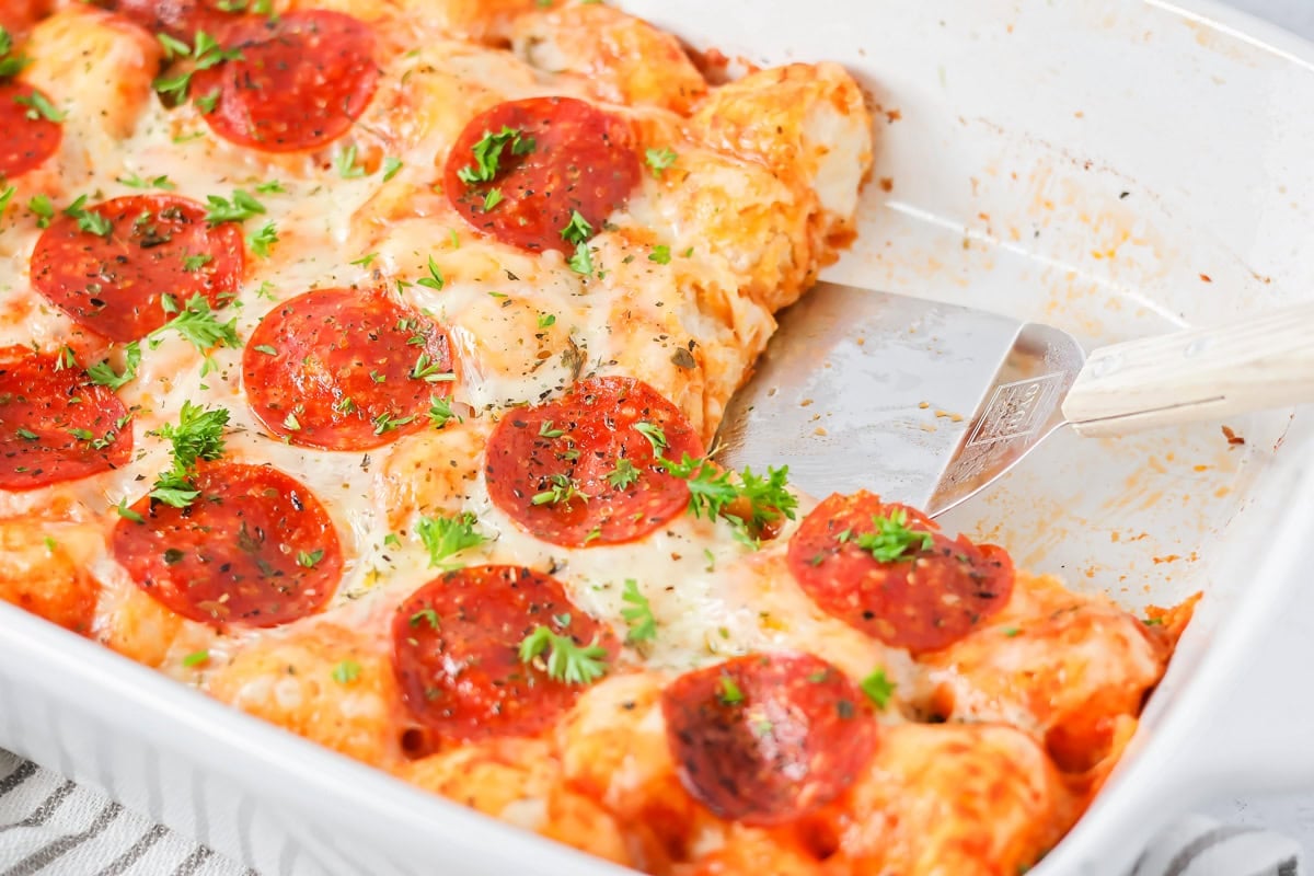 Easy cheesy pizza casserole is prepped in under 10 minutes and only requires 5 ingredients for a dinner win! Pizza casserole in baking dish with spatula scooping a piece out.