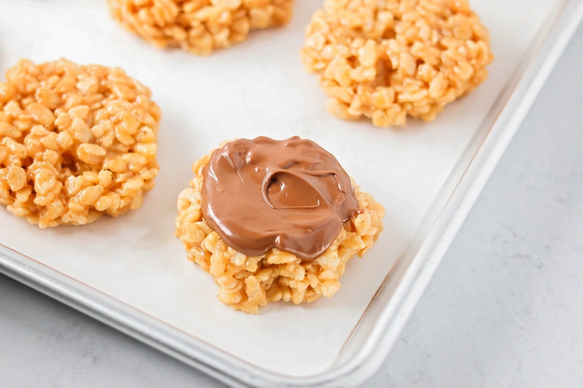 These scotcharoo cookies with crispy cereal, peanut butter, and a chocolate butterscotch topping are perfect for parties and evenings at home. Spreading melted chocolate over the flattened cookie balls.