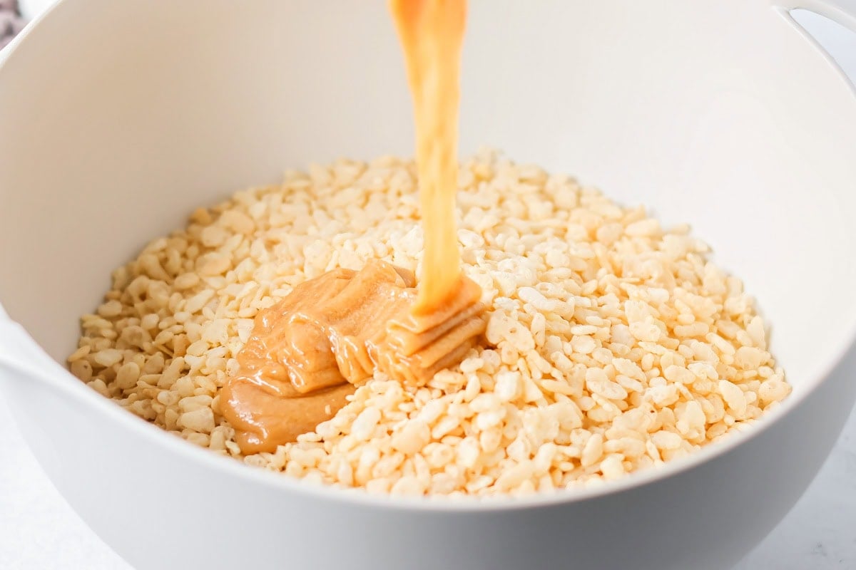 These scotcharoo cookies with crispy cereal, peanut butter, and a chocolate butterscotch topping are perfect for parties and evenings at home. Pouring peanut butter mixture over rice krispies.