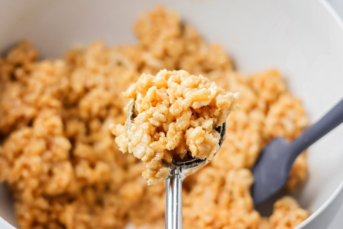 These scotcharoo cookies with crispy cereal, peanut butter, and a chocolate butterscotch topping are perfect for parties and evenings at home. Lifting the coated cereal with a spoon.