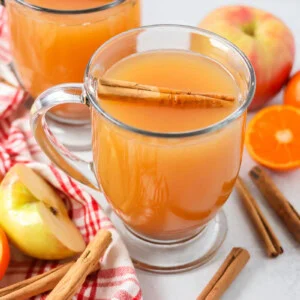 Homemade wassail recipe poured into glass with cinnamon sticks, apples and oranges.
