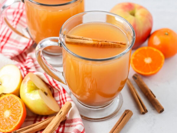Homemade wassail recipe poured into glass with cinnamon sticks, apples and oranges.
