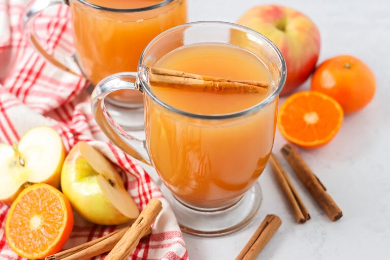 Homemade wassail recipe poured into glass with cinnamon sticks, apples and oranges.