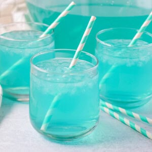 Blue punch recipe poured into glasses with ice and straws.