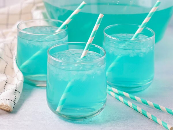 Blue punch recipe poured into glasses with ice and straws.