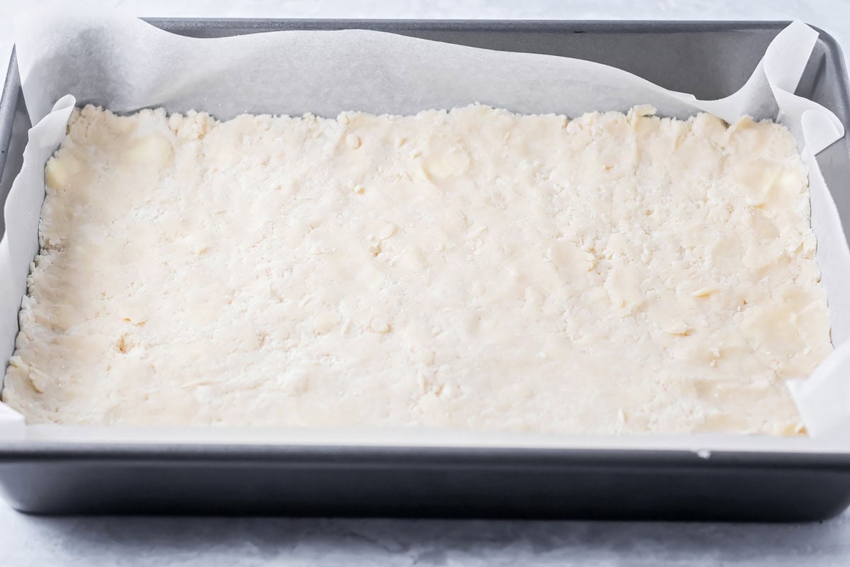 Shortbread crust spread in a lined baking dish.