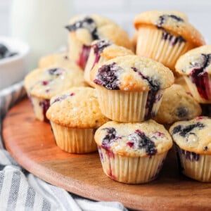 Mini blueberry muffins stacked on each other on wooden board.