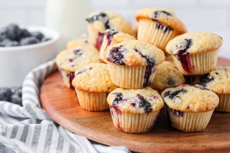 Mini blueberry muffins stacked on each other on wooden board.
