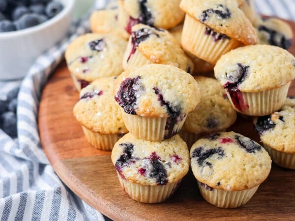Mini blueberry muffins stacked on each other on wooden board.