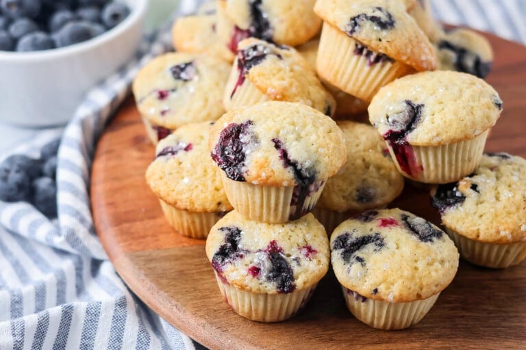 Mini blueberry muffins stacked on each other on wooden board.