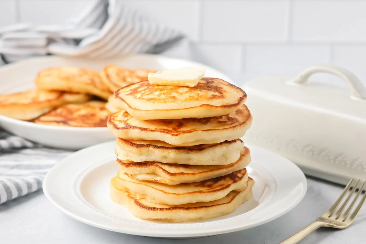 Homemade pancakes stacked on top of each other on white plate.