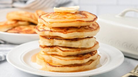 Easy pancake recipe stacked on top of each other on white plate with butter and syrup.