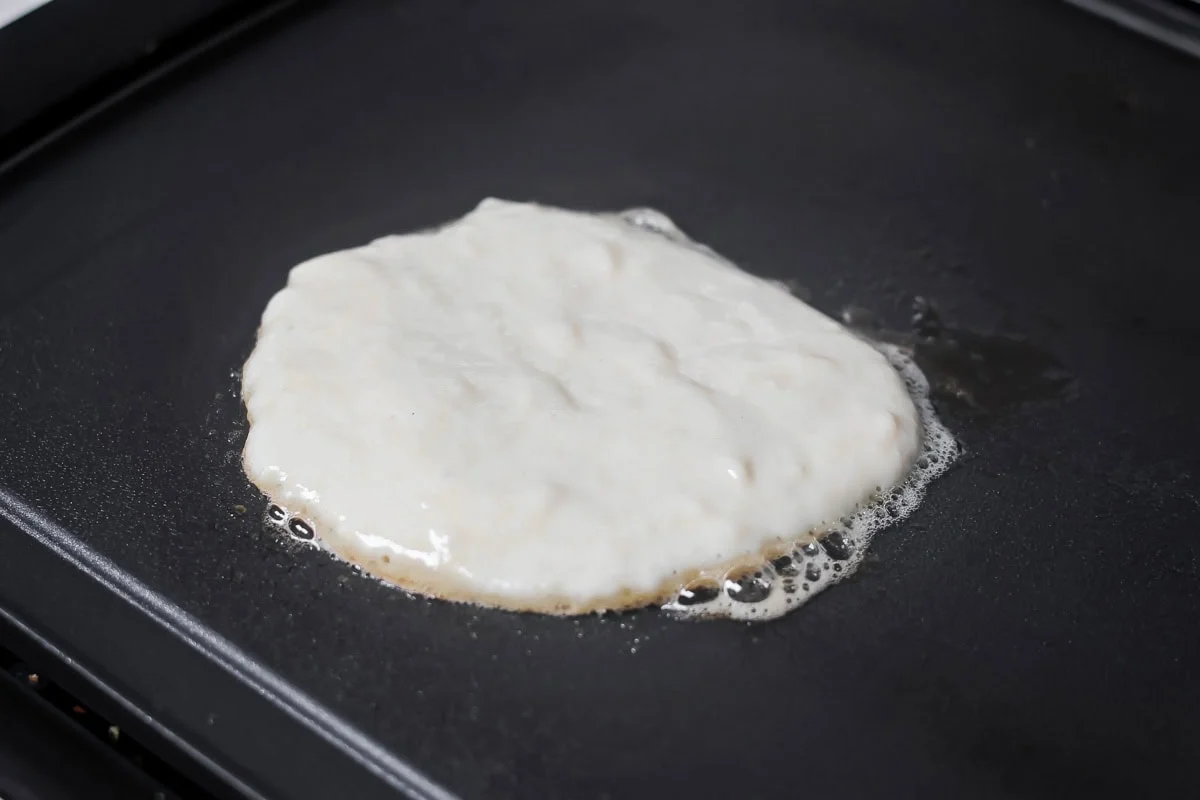 Pancake batter on griddle cooking up.