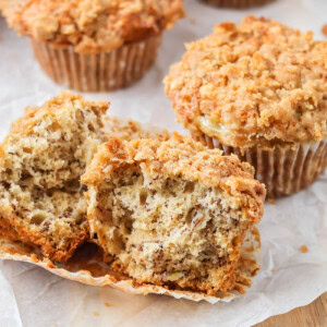Banana crumb muffins on parchment paper with one broken in half.