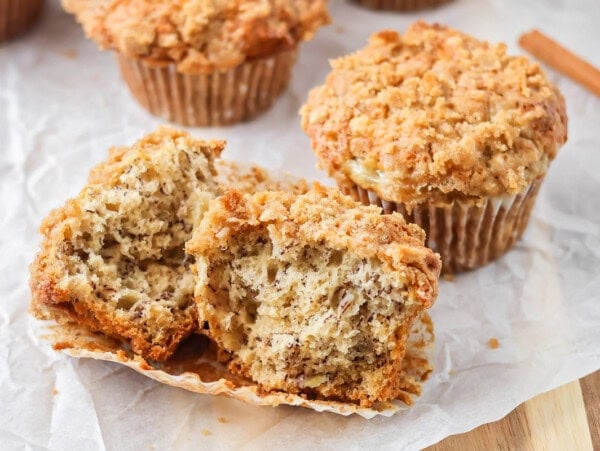 Banana crumb muffins on parchment paper with one broken in half.