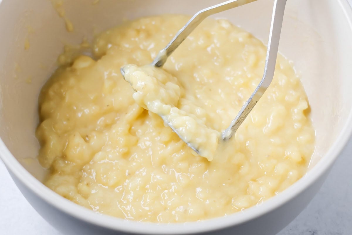 Mashing bananas in a white bowl for banana crumb muffins.