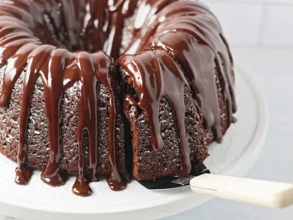 Brownie Cake recipe on cake stand with a slice being served.