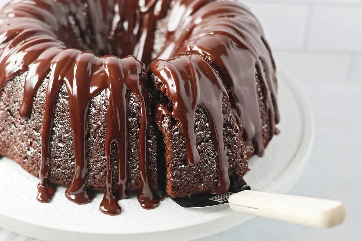 Brownie cake recipe with glaze on top with slice being served.