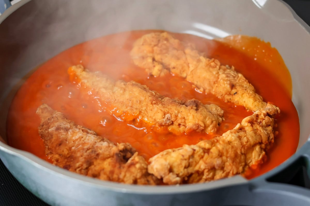 Dipping buffalo chicken tenders into a buffalo sauce.