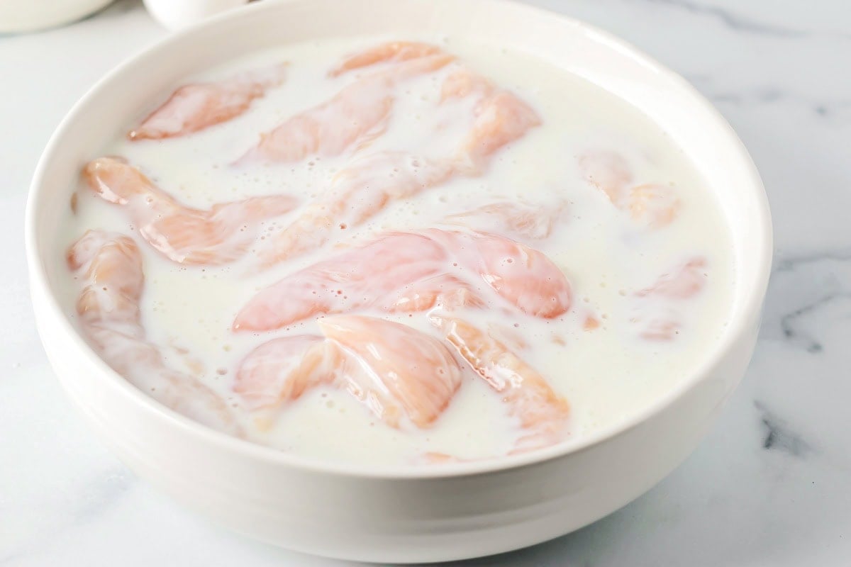 Buffalo chicken tenders in a bowl of buttermilk.