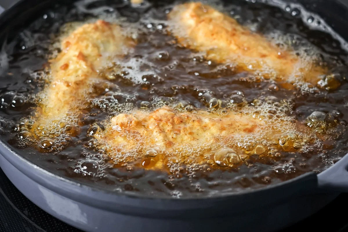 Frying buffalo chicken tenders in a pan of oil.