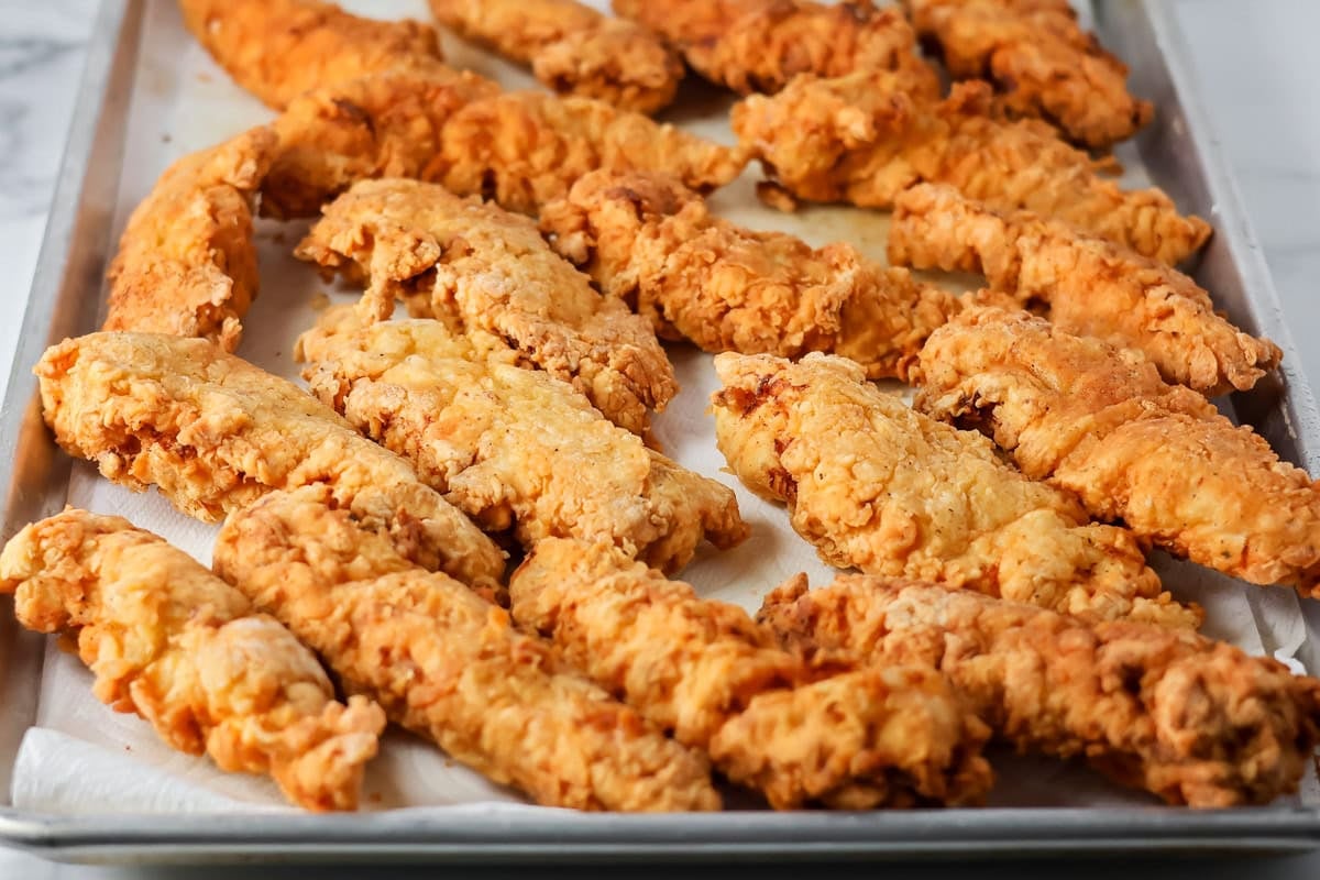 Fried buffalo chicken tenders on a paper towel lined sheet.