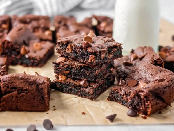 Cake Mix Brownies stacked on each other with glass of milk in the background.