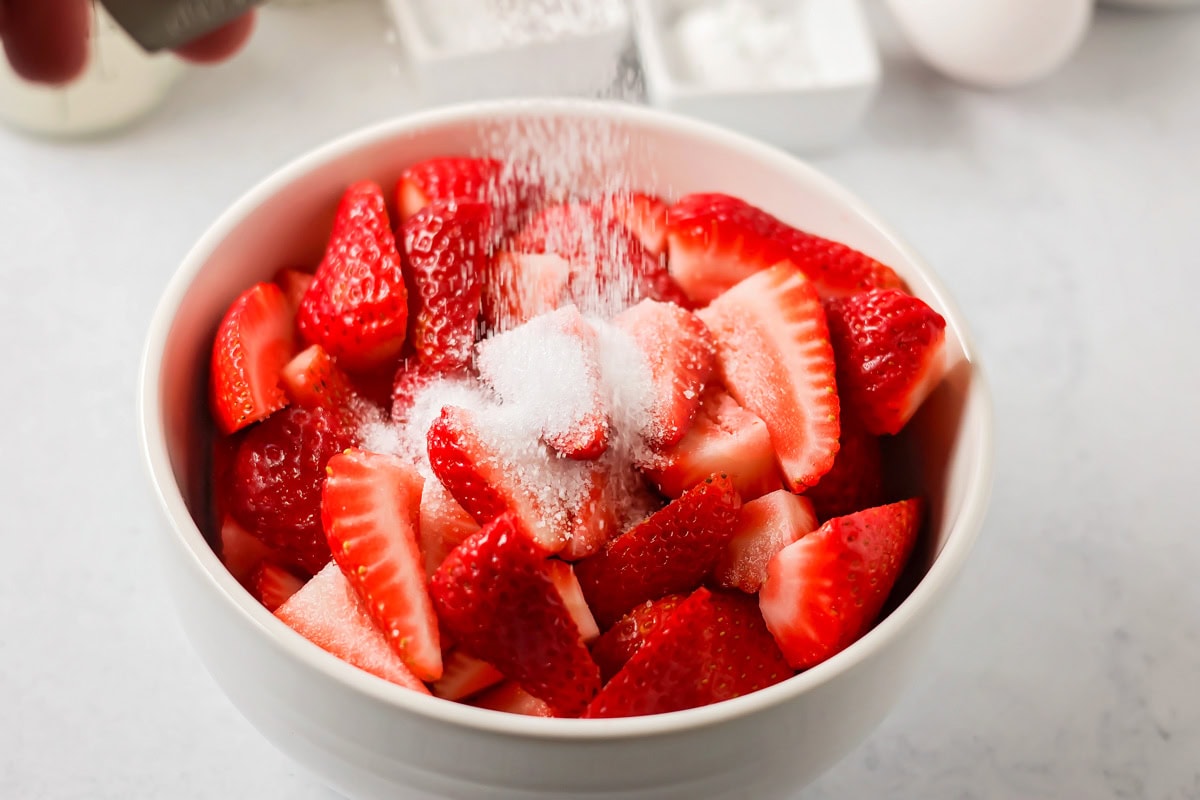 Adding sugar to a bowl of sliced strawberries for classic strawberry shortcake.
