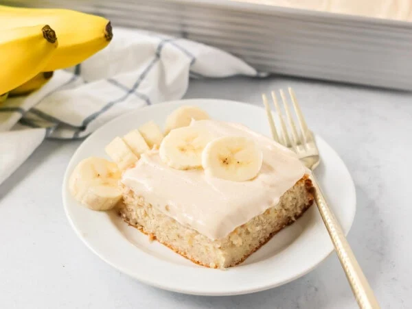 A slice of easy banana cake frosted and topped with fresh banana slices.