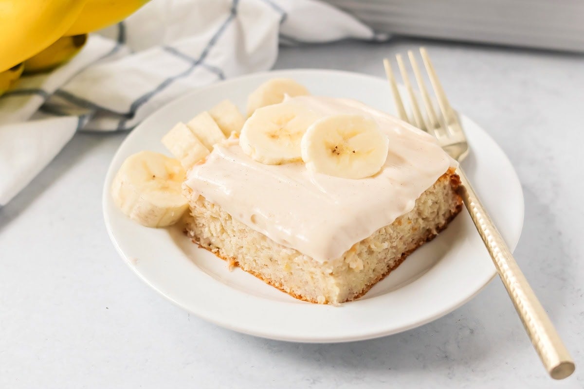 A square slice of easy banana cake topped with frosting and banana slices.