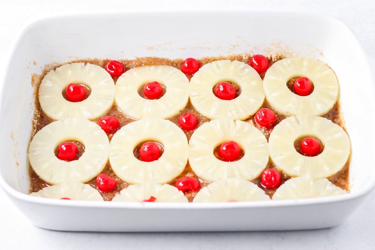 Placing brown sugar sauce, pineapple rings, and cherries on the bottom of a baking dish.