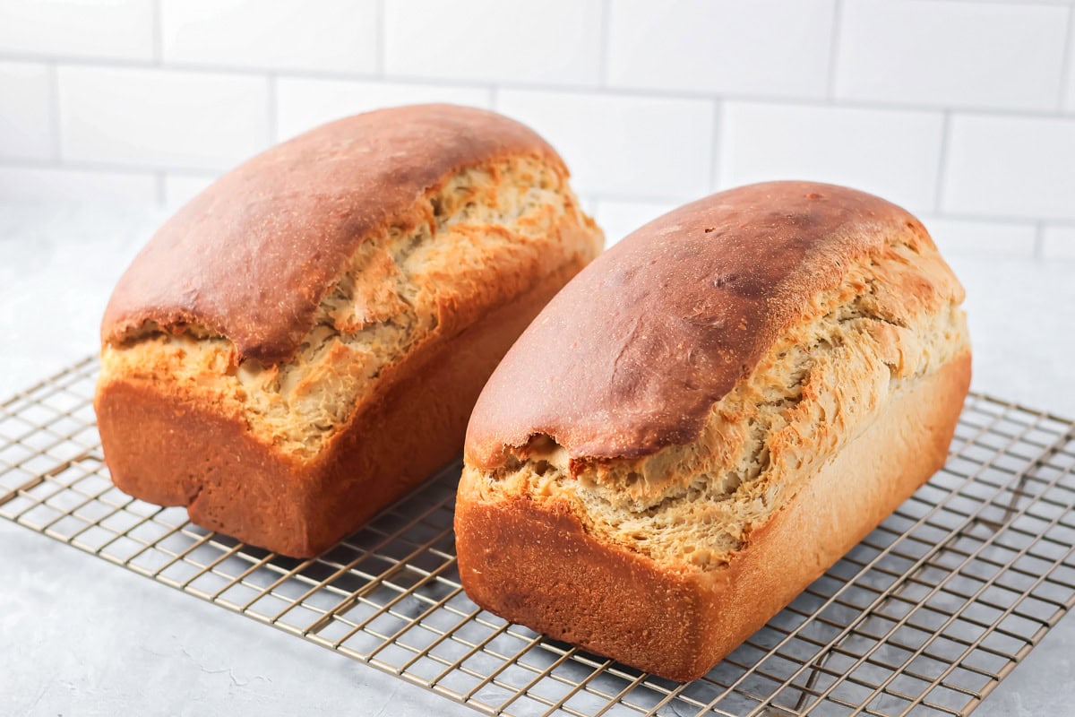 Two baked loaves of honey bread on a cooling rack.