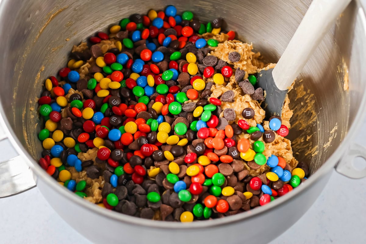 Adding chocolate chips and M&Ms to the cookie batter.