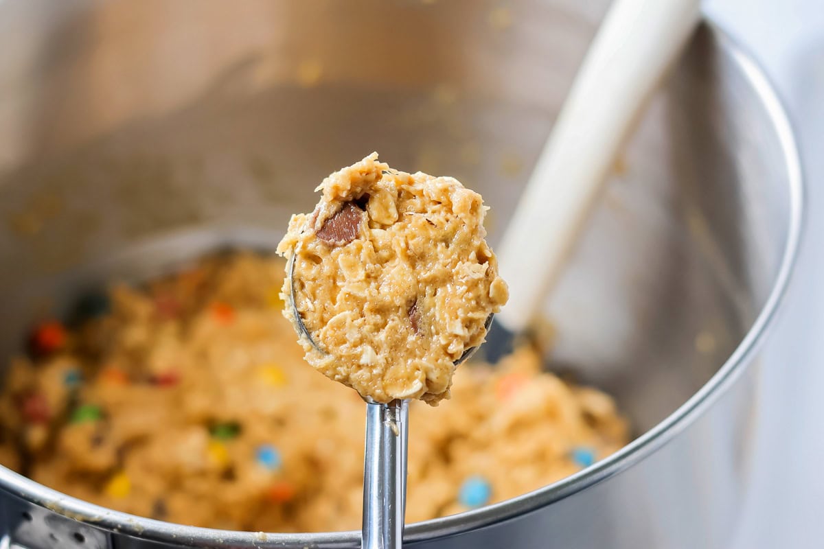 Scooping monster cookie dough from a metal bowl.