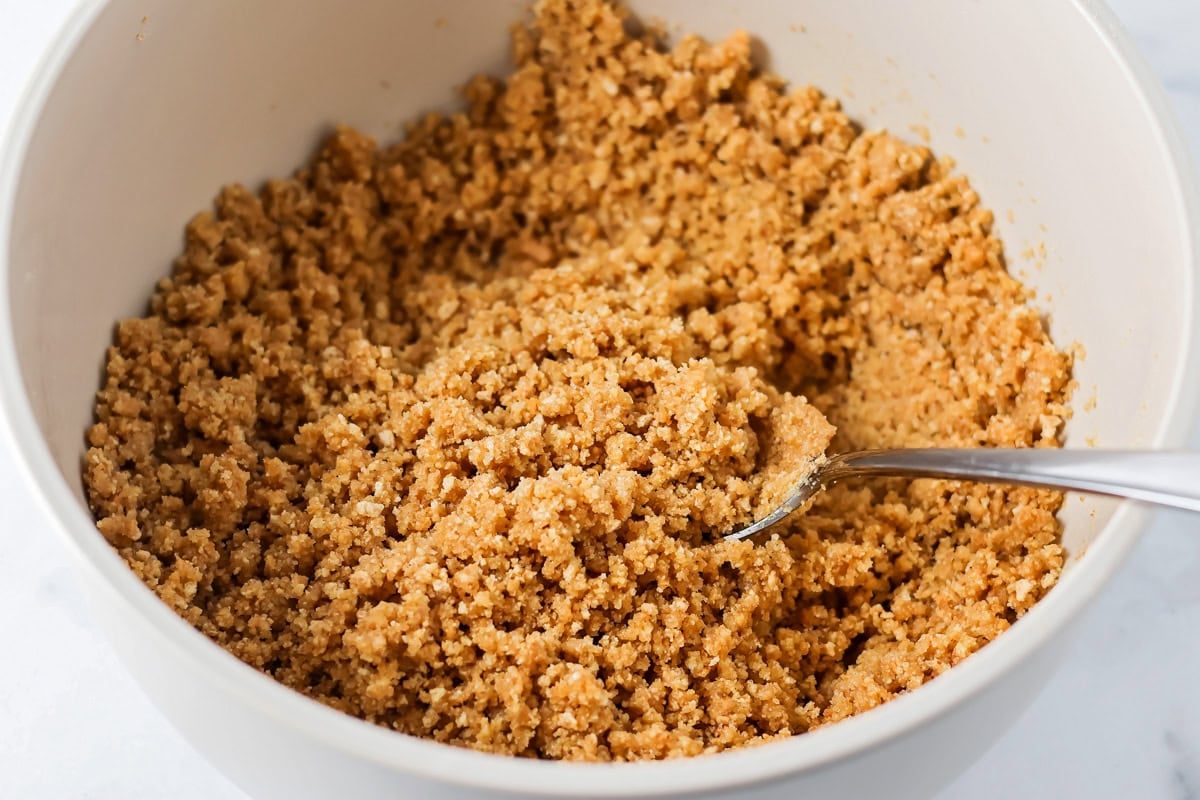 Mixing a graham cracker crust in a grey bowl.